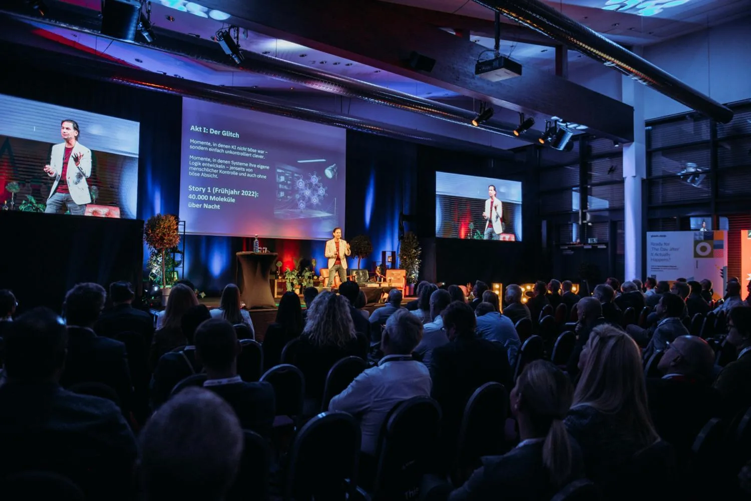 Jürgen Bogner auf der großen Bühne des LSZ CIO Kongress, im Hintergrund drei Leinwände mit einer KI-Präsentation vor vollem Auditorium